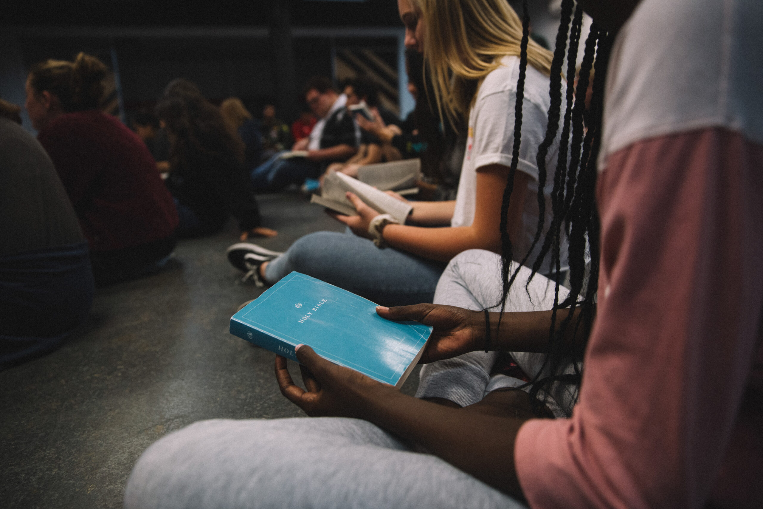 Young adults sitting at a Bible study in church looking at their bibles cropped with copy space
